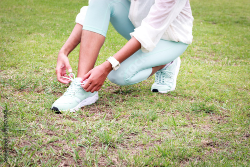 Athlete during running tying shoelaces on sneakers on green grass lawn, jogger training and doing workout at track and field stadium