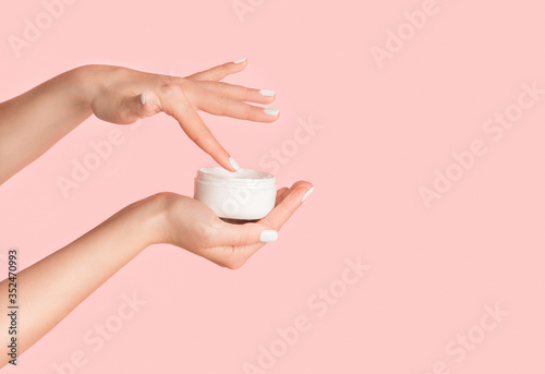 Fotografia Unrecognizable girl applying cream from jar onto her hands against pink backgrou