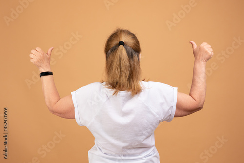 Female in white blank t-shirt standing back to the camera with raised hands, holding thumbs up