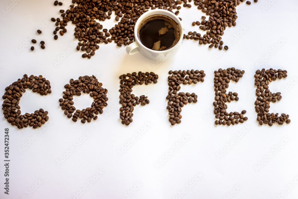 Cup of black coffee on white background with letter coffee wrote from fresh rosted beans. White cup of coffee and letters Coffee. Brown coffee letters isolated on a white background. Copy-space. Cup of black coffee on white background with letter coffee wrote from fresh rosted beans. White cup of coffee and letters Coffee. Brown coffee letters isolated on a white background. Copy-space.