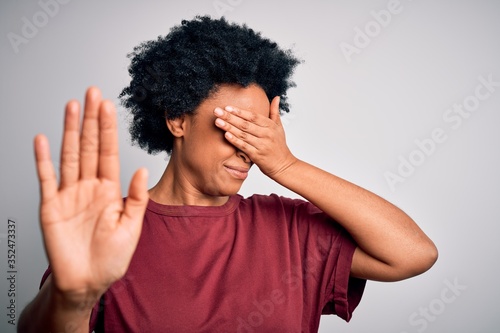 Young beautiful African American afro woman with curly hair wearing casual t-shirt standing covering eyes with hands and doing stop gesture with sad and fear expression. Embarrassed and negative