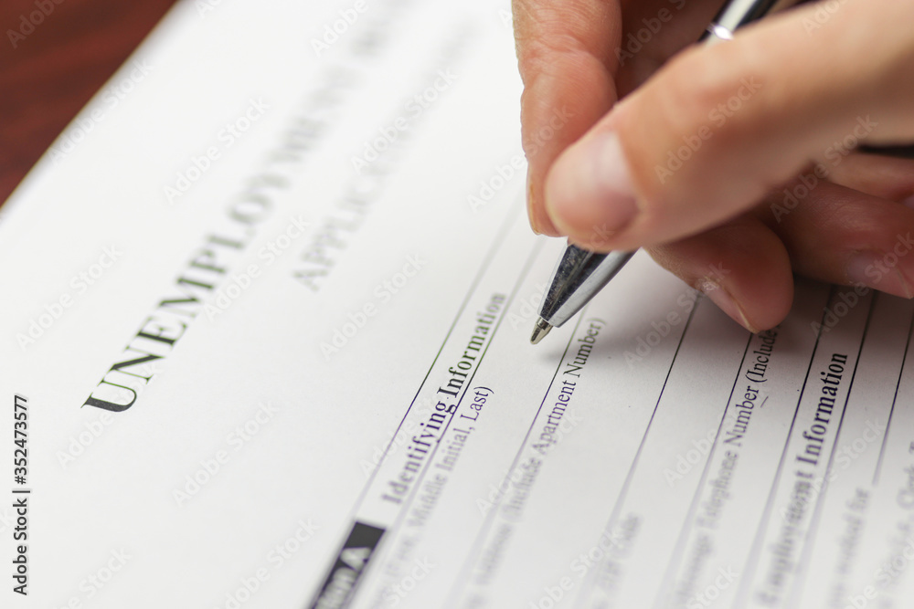 Close-up of a person's hand filing social security benefits application form. Concept of Covid-19 coronavirus and stay at home order impact on economy, world economic crisis, unemployment. Close-up of a person's hand filing social security benefits application form. Concept of Covid-19 coronavirus and stay at home order impact on economy, world economic crisis, unemployment.