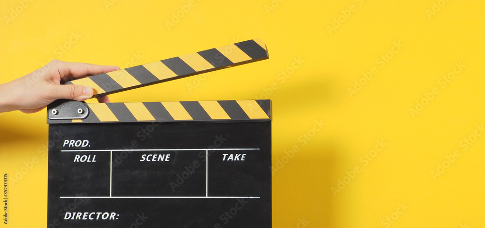 Hand is holding black&yellow clapper board or movie slate.It is used in video production and film industry on yellow background.