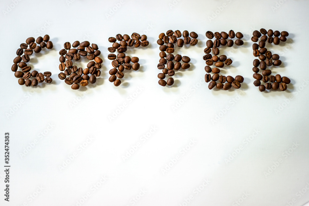 Word coffee made from coffee beans. A word from coffee roasted grains on a white background. Roasted coffee beans in shape of alphabets, coffee. Brown coffee beans isolated on white board. Copy-space.