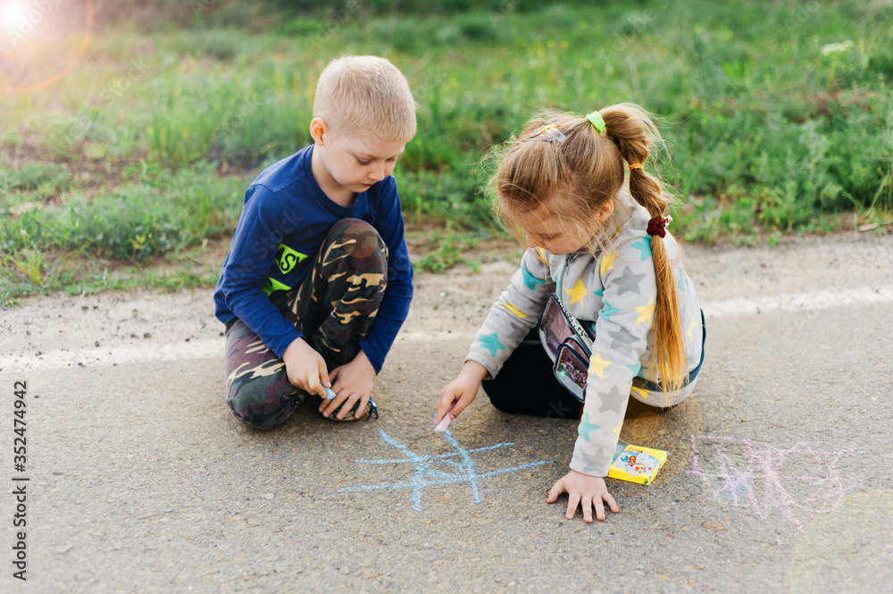 Beautiful boy and girl twins draw on the pavement with colored crayons. International Children's Day. Beautiful boy and girl twins draw on the pavement with colored crayons. International Children's Day.