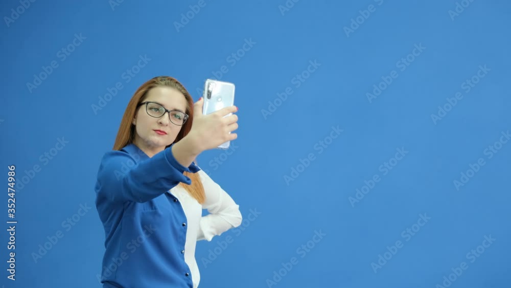 Cheerful girl takes a selfie on a smartphone camera on the blue background Cheerful girl takes a selfie on a smartphone camera on the blue background