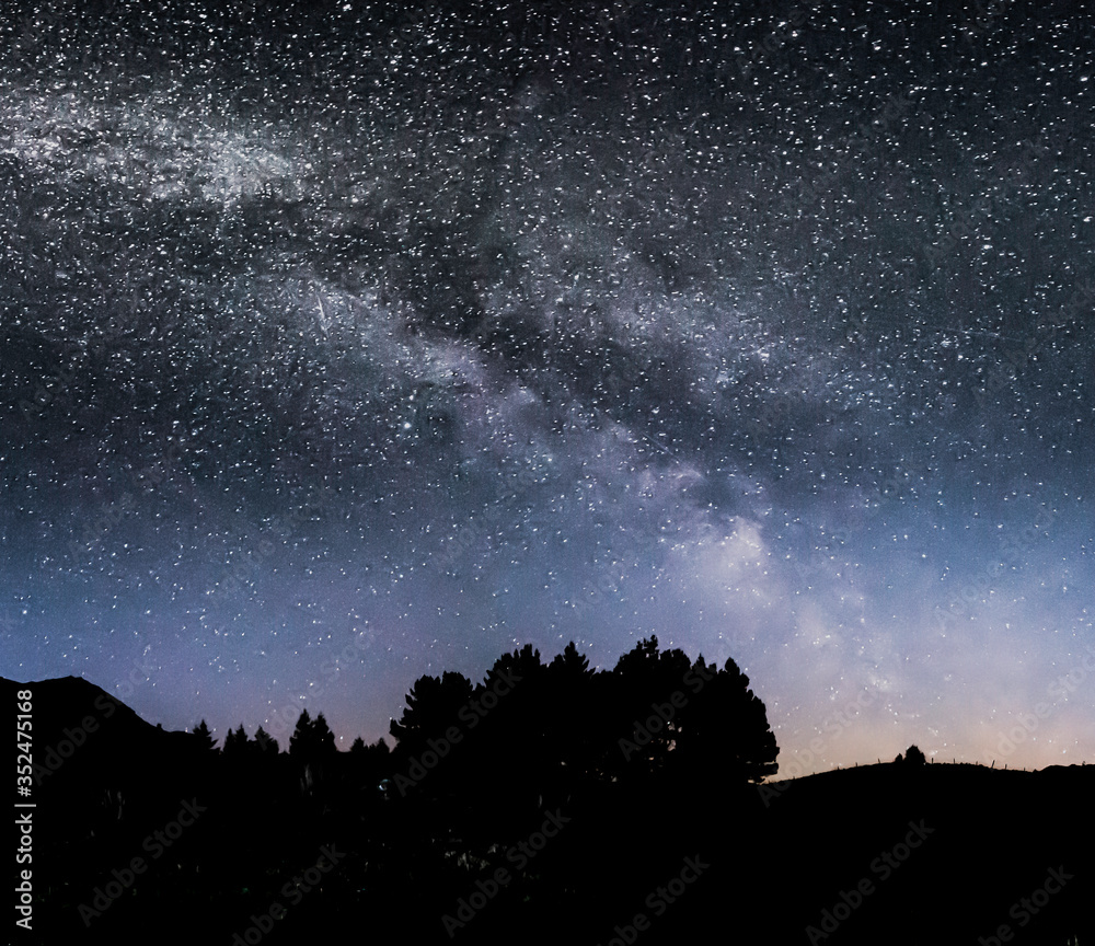 Milky way constellation above silhouetted trees and hills.Beautiful night landscape scene in Lake District, Cumbria, UK.Galactic bridge and sky full of stars in british wilderness.