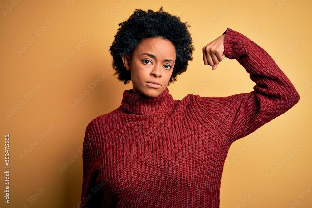 Young beautiful African American afro woman with curly hair wearing casual turtleneck sweater Strong person showing arm muscle, confident and proud of power Young beautiful African American afro woman with curly hair wearing casual turtleneck sweater Strong person showing arm muscle, confident and proud of power