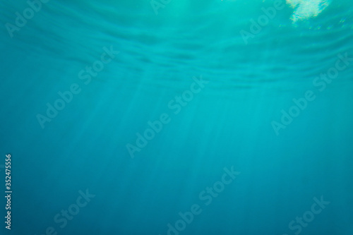 blue ocean surface seen from underwater. waves underwater and rays of sunlight shining through