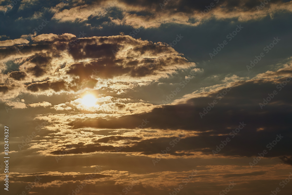 Beautiful blue sunset sky with a yellow sun that shines through the clouds