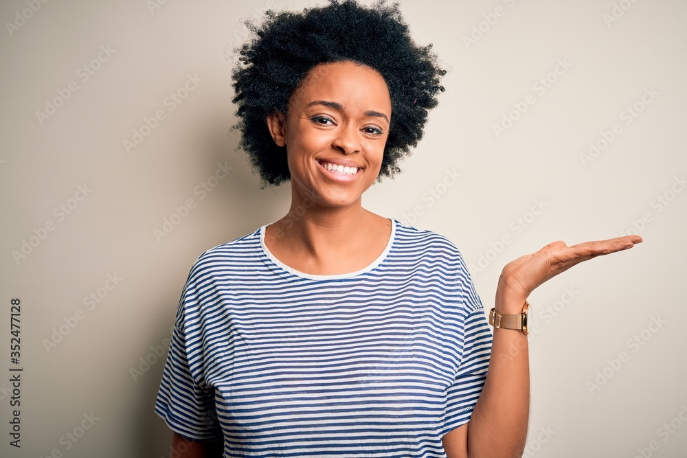 Young beautiful African American afro woman with curly hair wearing striped t-shirt smiling cheerful presenting and pointing with palm of hand looking at the camera. Young beautiful African American afro woman with curly hair wearing striped t-shirt smiling cheerful presenting and pointing with palm of hand looking at the camera.