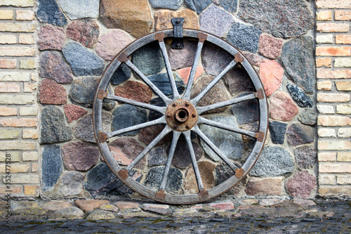 Historical vehicle wheel attached to a wall made of stones and used as decorative element.
