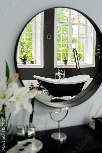 Black and white modern bathroom with silver fittings with large sunny windows, reflection in the mirror. Interior design concept. Soft selective focus.