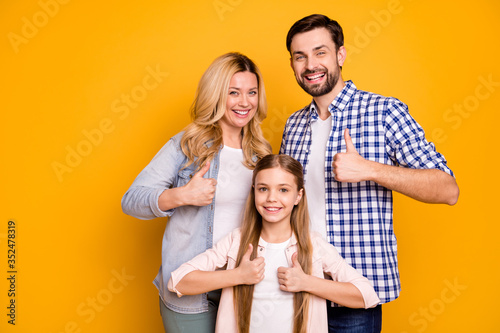 Photo wife beautiful mom lady handsome husband dad guy couple little school girl daughter happy together raise thumb fingers up wear casual clothes isolated yellow color background © deagreez