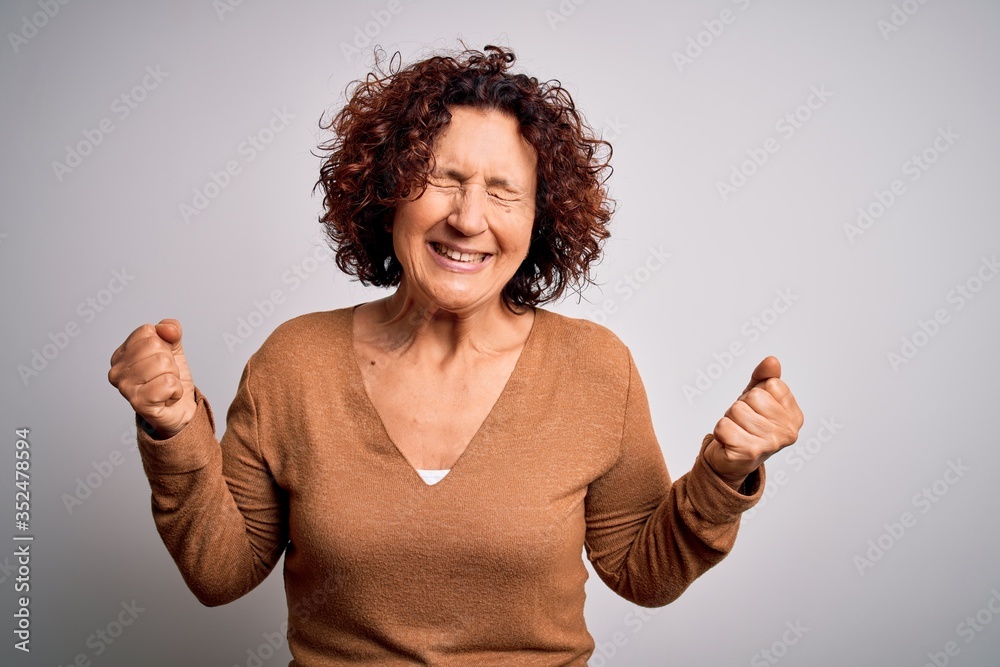 Middle age beautiful curly hair woman wearing casual sweater over isolated white background very happy and excited doing winner gesture with arms raised, smiling and screaming for success. Celebrate Middle age beautiful curly hair woman wearing casual sweater over isolated white background very happy and excited doing winner gesture with arms raised, smiling and screaming for success. Celebrate