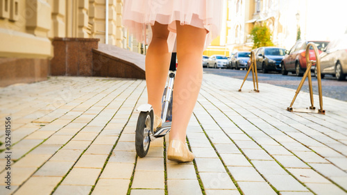 Closeup photo of beautfiul female feet standing on kick scooter on city street