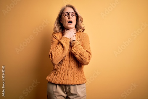 Middle age beautiful blonde woman wearing casual sweater and glasses over yellow background shouting suffocate because painful strangle. Health problem. Asphyxiate and suicide concept.