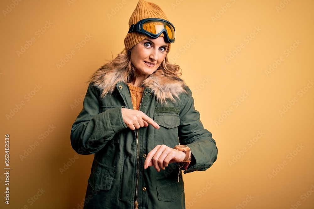 Middle age beautiful blonde skier woman wearing snow sportwear and ski goggles In hurry pointing to watch time, impatience, upset and angry for deadline delay Middle age beautiful blonde skier woman wearing snow sportwear and ski goggles In hurry pointing to watch time, impatience, upset and angry for deadline delay