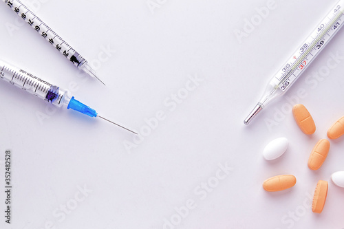 Pills, syringe and thermometer on a white background. Pills, medicine and health. Virus protection concept. Flat lay, top view, copy space.