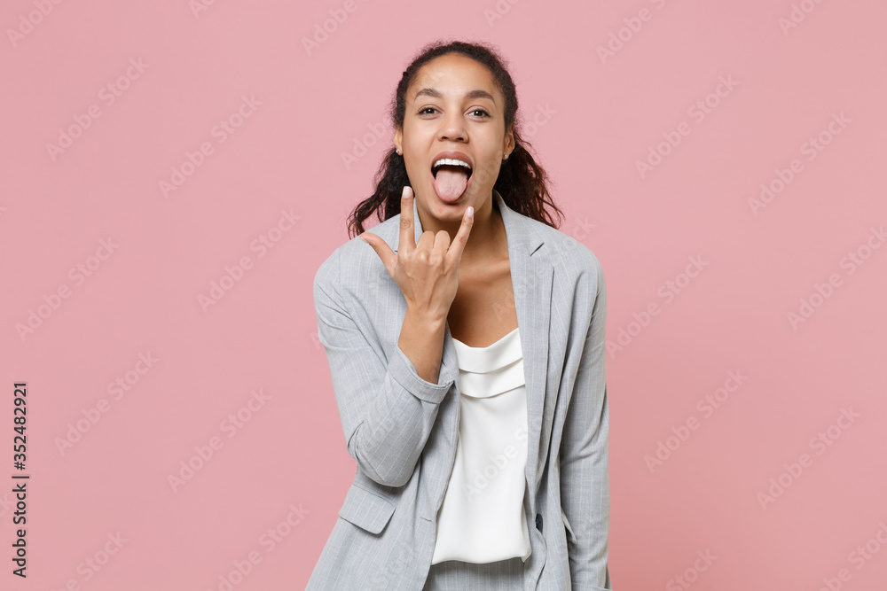 Cheerful young african american business woman in grey suit white shirt isolated on pink wall background. Achievement career wealth business concept. Depicting heavy metal rock sign, horns up gesture. Cheerful young african american business woman in grey suit white shirt isolated on pink wall background. Achievement career wealth business concept. Depicting heavy metal rock sign, horns up gesture.
