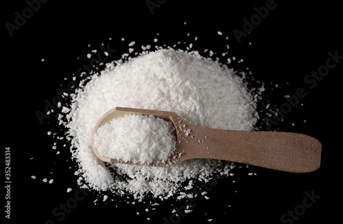 Shredded coconut meat, powder pile with wooden spoon isolated on black background