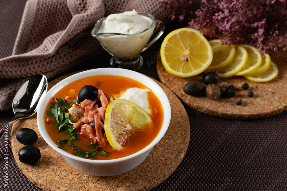 Soup Solyanka is a combined meat soup with smoked meat , various types of meat and tomato paste, serving dishes with sour cream, lemon and fresh herbs. Black olives on the table and a sprig of fresh f Soup Solyanka is a combined meat soup with smoked meat , various types of meat and tomato paste, serving dishes with sour cream, lemon and fresh herbs. Black olives on the table and a sprig of fresh f