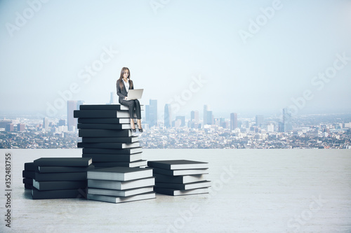 Young businesswoman with laptop sitting on book pile
