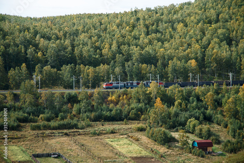A train rides on rails past residential buildings in the countryside