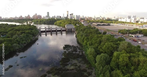 4K cloudy afternoon aerial scenic footage of Mnevniki hydro system dam regulating Moscow River water levels overlooking green park, distant city sky scrapers in Krylatskoye area in Moscow, Russia photo