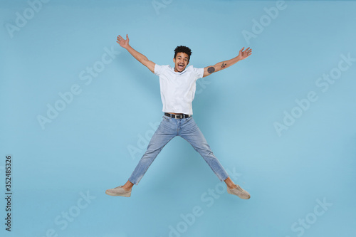 Wallpaper Mural Excited young african american guy in casual white t-shirt posing isolated on pastel blue background studio portrait. People lifestyle concept. Mock up copy space. Jumping, spreading hands and legs. Torontodigital.ca