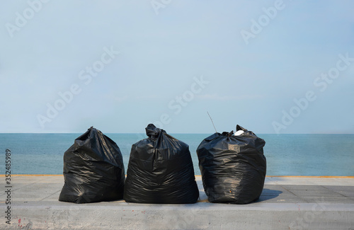 Three big garbage bags are on a pavement by the beach.  Surrounding is clean and tidy. Blue sky and sea are in blurred background.  Trash, waste management, object, outdoor.  Copy space.