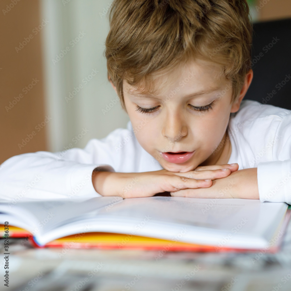 Little blonde school kid boy reading a book at home. Child interested in reading magazine for kids. Leisure for kids, building skills and education concept Little blonde school kid boy reading a book at home. Child interested in reading magazine for kids. Leisure for kids, building skills and education concept
