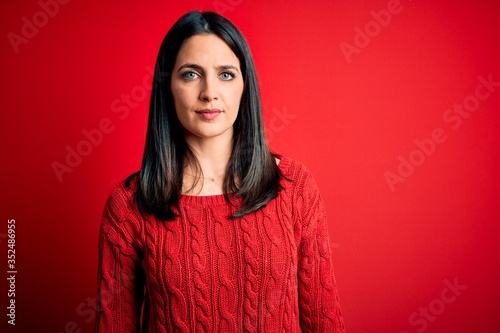 Young brunette woman with blue eyes wearing casual sweater over isolated red background Relaxed with serious expression on face. Simple and natural looking at the camera.