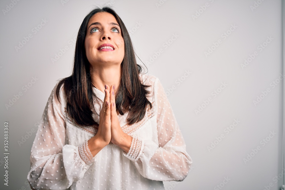 Young brunette woman with blue eyes wearing casual t-shirt over isolated white background begging and praying with hands together with hope expression on face very emotional and worried. Begging. Young brunette woman with blue eyes wearing casual t-shirt over isolated white background begging and praying with hands together with hope expression on face very emotional and worried. Begging.