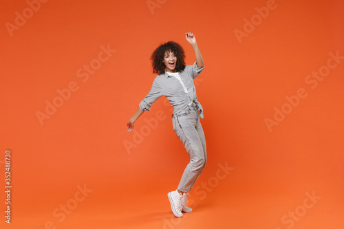 Funny young african american woman girl in gray casual clothes posing isolated on orange background in studio. People lifestyle concept. Mock up copy space. Dancing, standing on toes, rising hands. © ViDi Studio