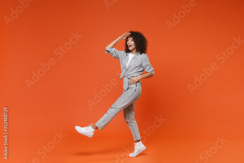 Excited young african american woman girl in gray casual clothes posing isolated on orange background. People lifestyle concept. Mock up copy space. Holding hand at forehead looking far away distance.