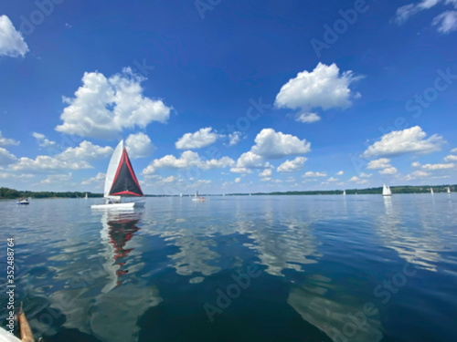 Sailboat on beautiful lake on blue sky and pleasant green landscape background and lovely reflection on water surface. Sailing is a popular sport and activity. Blurred view