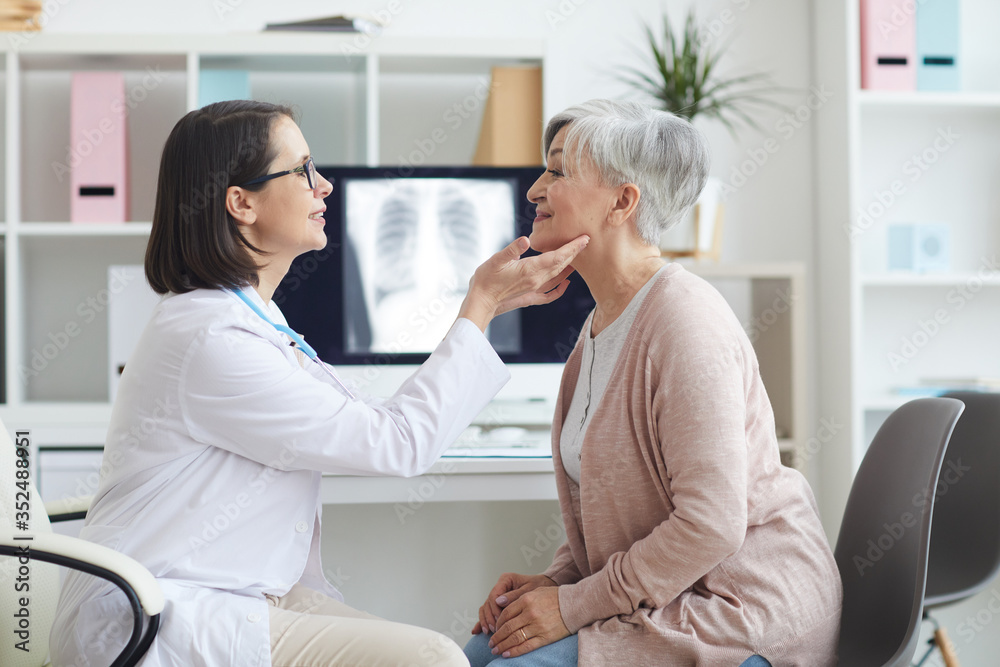 Obraz premium Side view portrait of young female doctor examining senior woman during consultation in med clinic