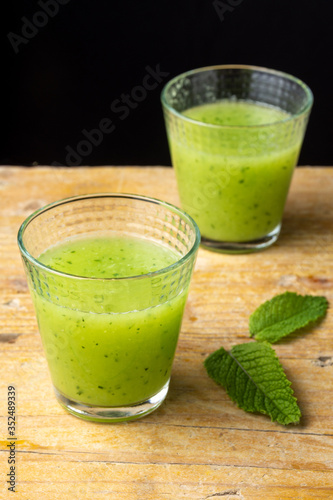 Top view of two glasses of cucumber juice with mint leaves on rustic table, black background, vertical