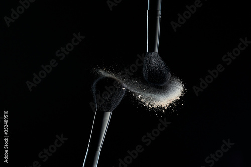 Makeup brushes with colorful powder explosion on black background. High speed photography of cosmetics.
