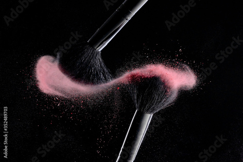 Makeup brushes with colorful powder explosion on black background. High speed photography of cosmetics.
