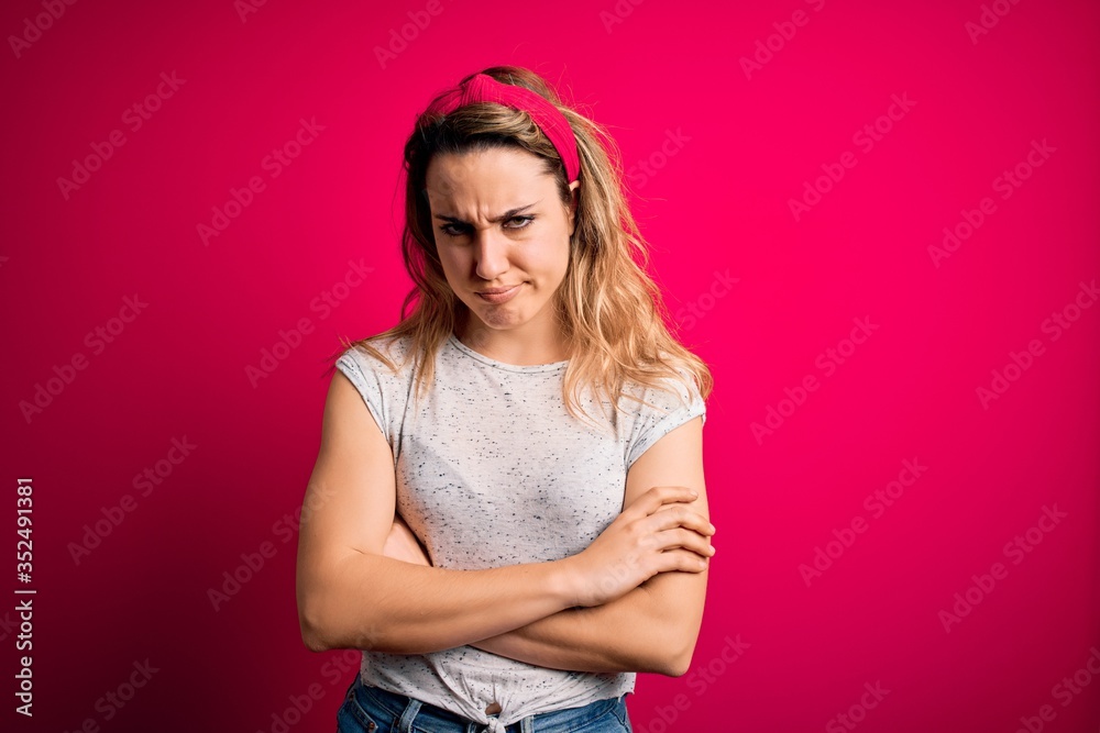 Young beautiful blonde woman wearing casual t-shirt standing over isolated pink background skeptic and nervous, disapproving expression on face with crossed arms. Negative person.