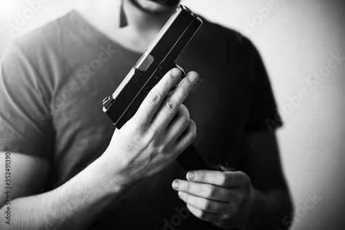 A black-and-white image of a man in a t-shirt holding a gun and replacing it with a magazine with cartridges. Danger. Army. Killer.