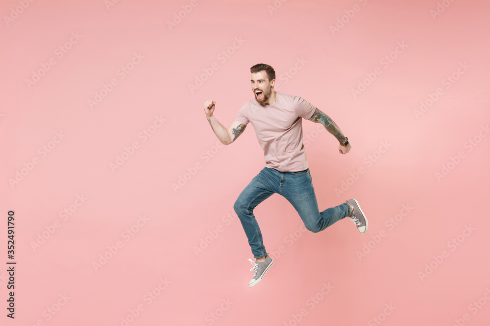 Excited young tattooed man guy in pastel casual t-shirt posing isolated on pink wall background studio portrait. People sincere emotions lifestyle concept. Mock up copy space. Jumping like running.