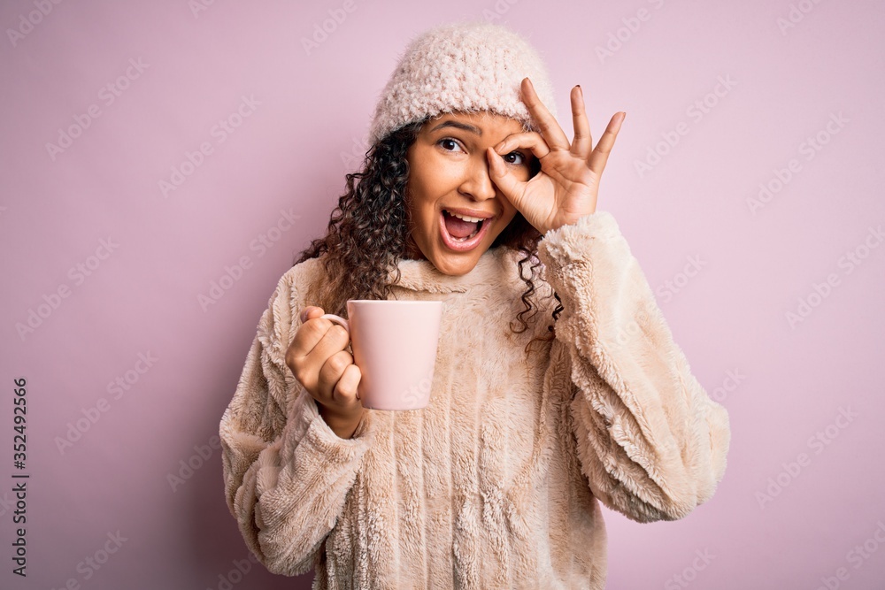 Young beautiful woman with curly hair drinking mug of coffee over isolated pink background with happy face smiling doing ok sign with hand on eye looking through fingers Young beautiful woman with curly hair drinking mug of coffee over isolated pink background with happy face smiling doing ok sign with hand on eye looking through fingers