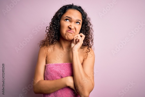 Young beautiful woman with curly hair wearing shower towel after bath over pink background with hand on chin thinking about question, pensive expression. Smiling with thoughtful face. Doubt concept.