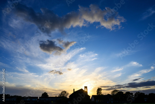 Dramatic clouds at sunset over St Johns Church in Beckenham, Kent, UK. The setting sun shines through the bell tower of the church. Beautiful clouds and evening sky at sunset with church silhouette.