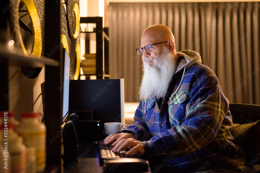 Mature bald bearded hipster man working overtime at home late at night