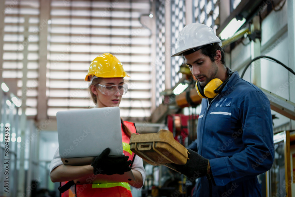 Industrial engineer worker woman and man wearing helmet discussing and working together with robot arm for arduino mechanism at manufacturing plant factory, young people working in industry