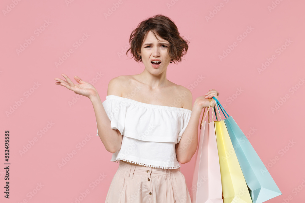 Displeased perplexed young woman girl in summer clothes hold package bag with purchases isolated on pink wall background in studio. Shopping discount sale concept. Mock up copy space. Spreading hands. Displeased perplexed young woman girl in summer clothes hold package bag with purchases isolated on pink wall background in studio. Shopping discount sale concept. Mock up copy space. Spreading hands.